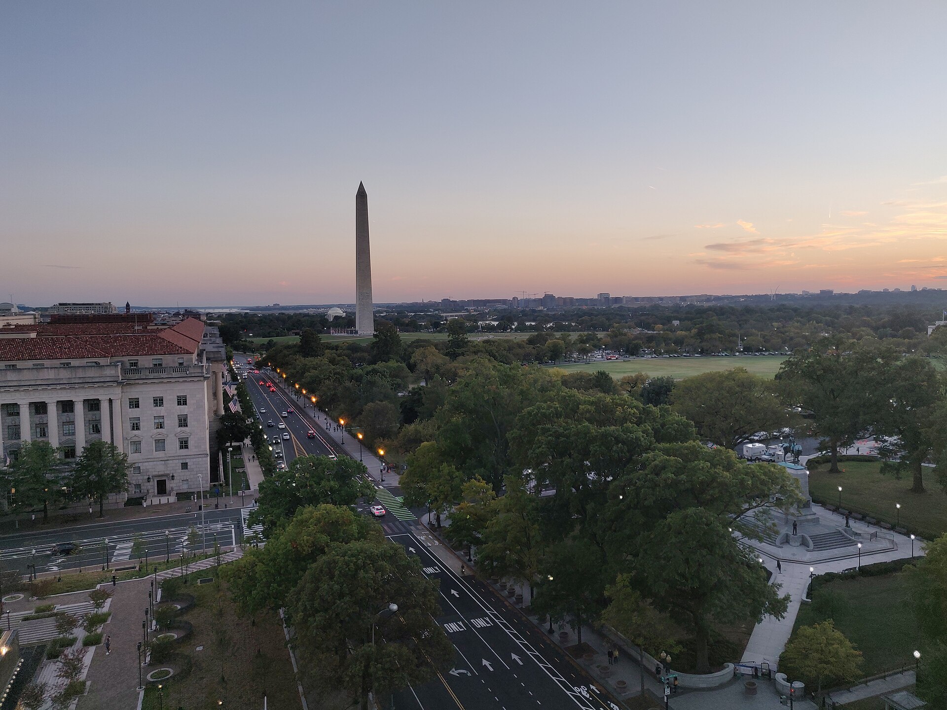The Washington Monument and National Mall at dusk, seen over tree-lined Constitution Avenue